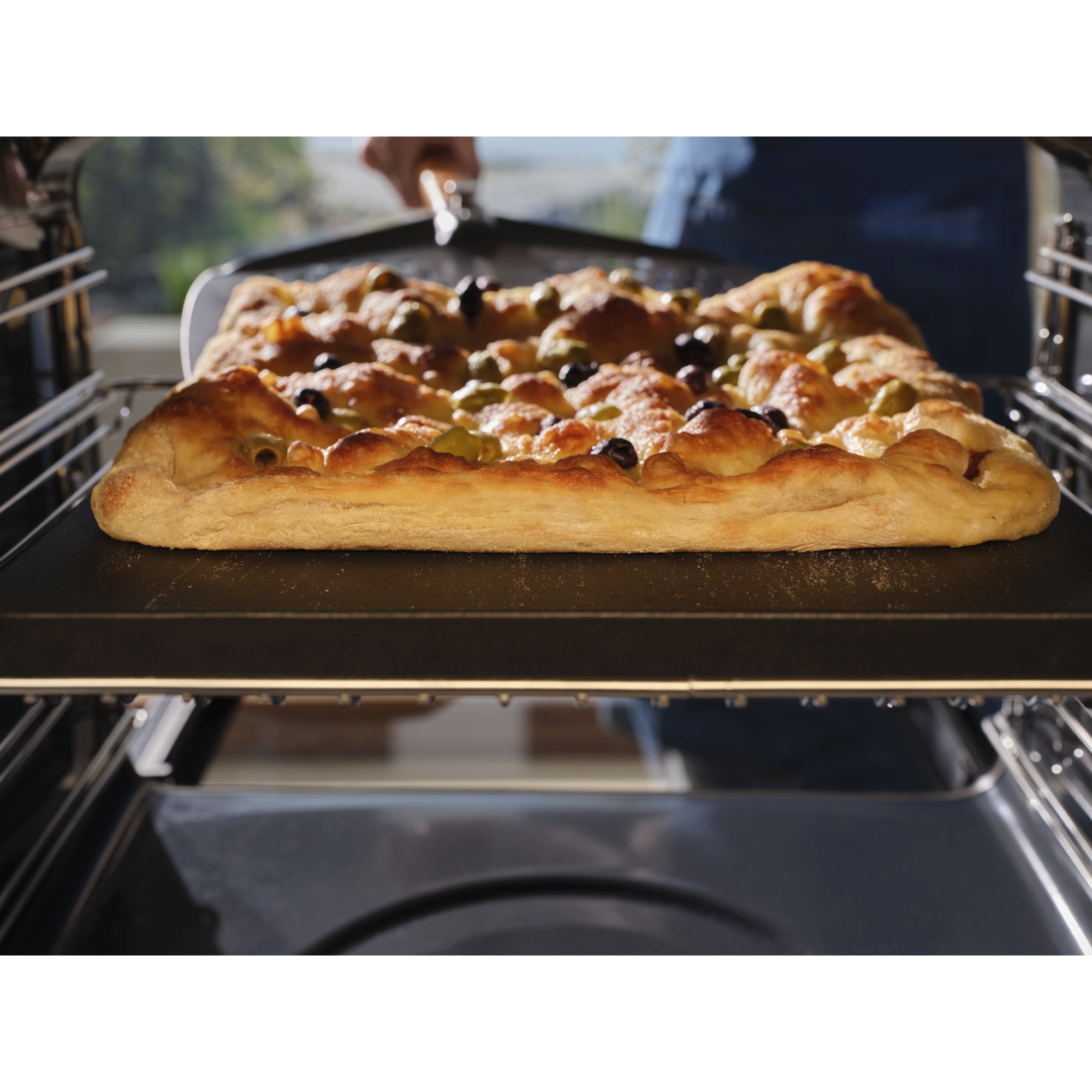A focaccia baking inside the pizza expert oven with a pizza peel underneath 