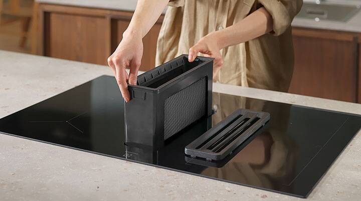 Hænder der sætter et fedtfilter på plads i en emhætte