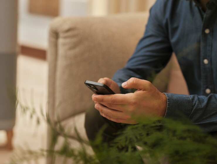 Mand der sidder ved siden af en luftrenser og holder en telefon.