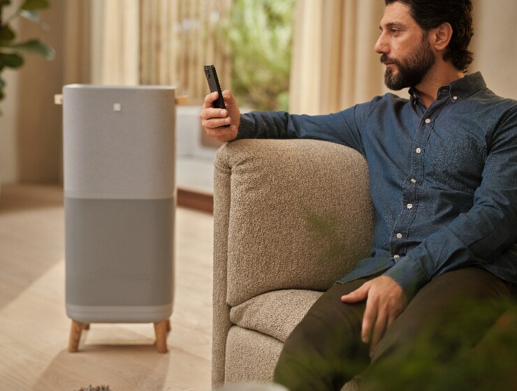Mand der sidder ved siden af en luftrenser og holder en telefon.