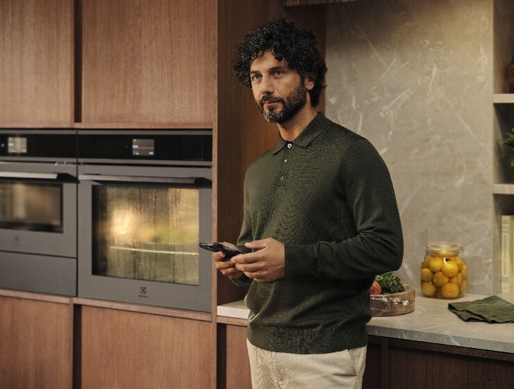 Mand der står i køkkenet og holder en telefon.