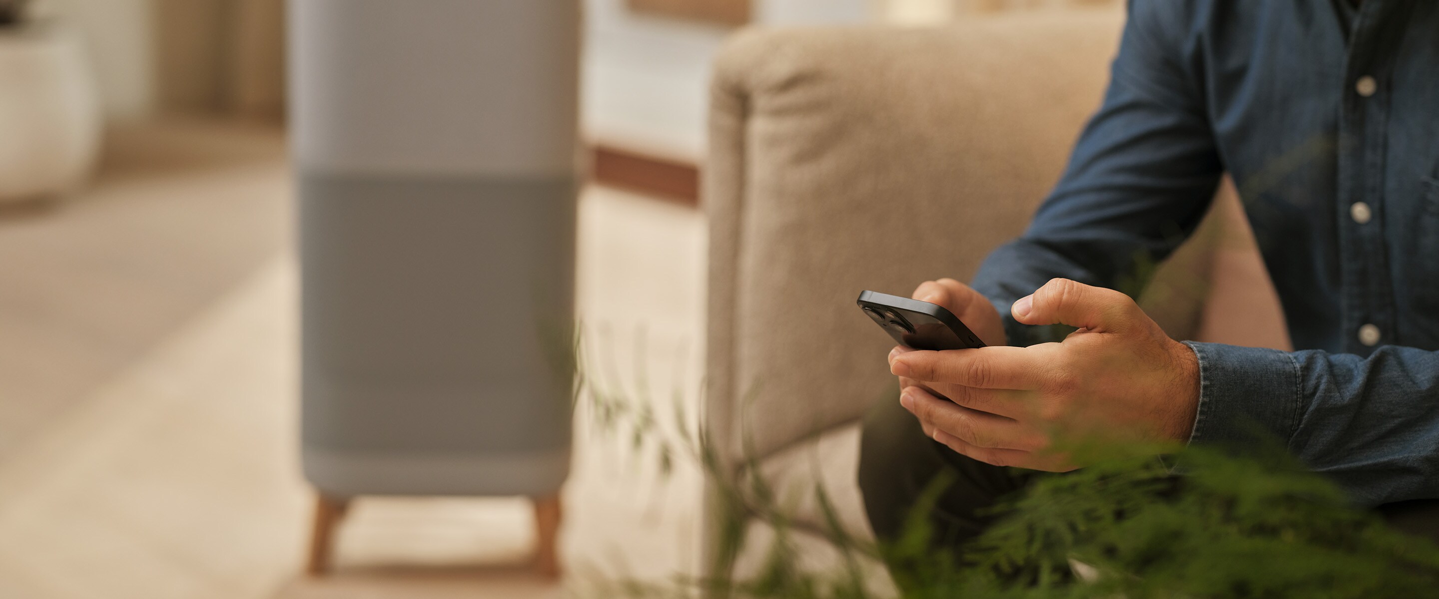 En mand sidder og holder en telefon. Luftrenser i baggrunden.