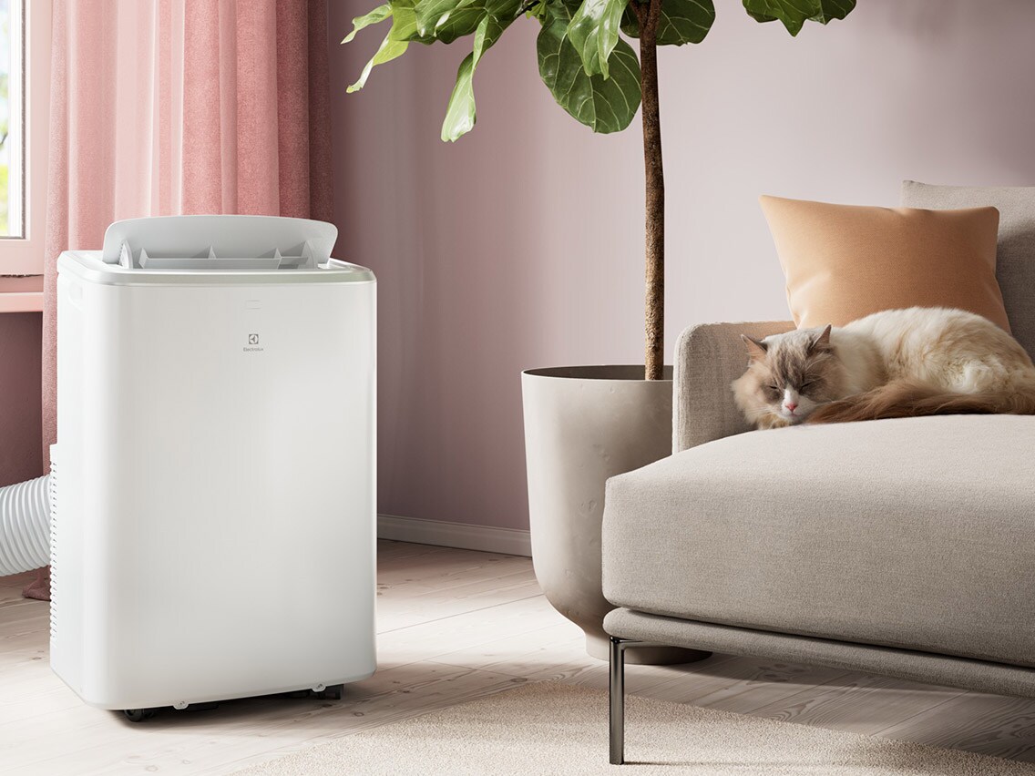 En hvid mobil Electrolux-aircondition i en lys stue hvor en kat sover i sofaen.