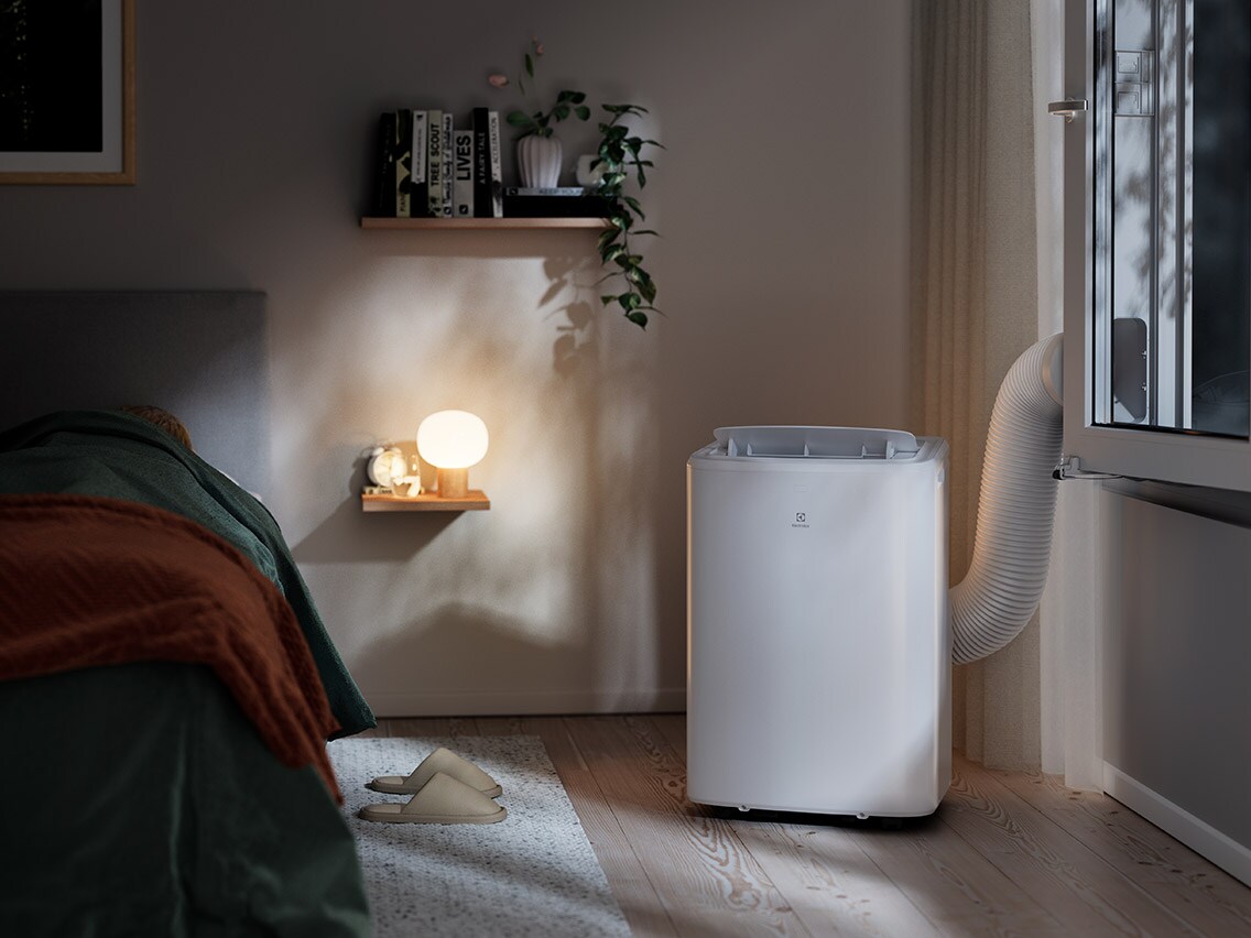 Hvid transportabel Electrolux-airconditioner med vindueskit i et soveværelse.