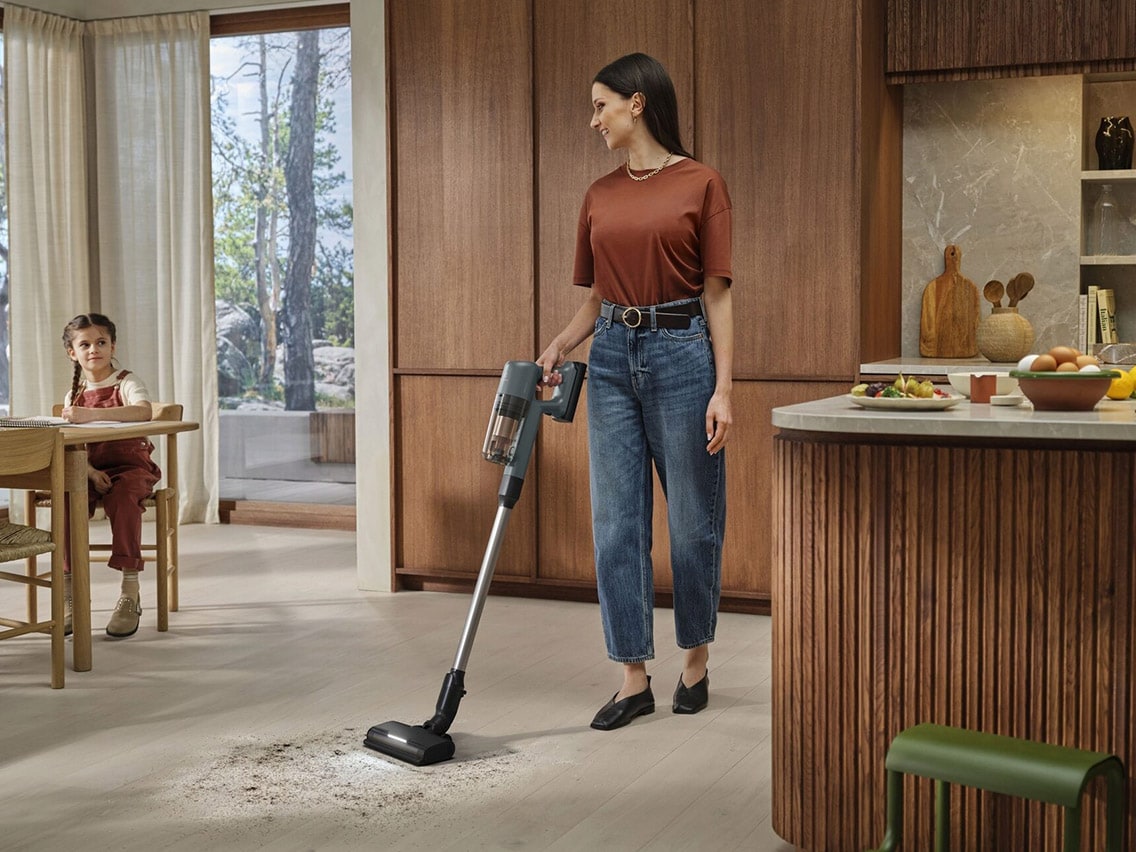 En kvinde bruger en trådløs Electrolux 700-støvsuger til at gøre rent på et lyst trægulv i et moderne køkken.
