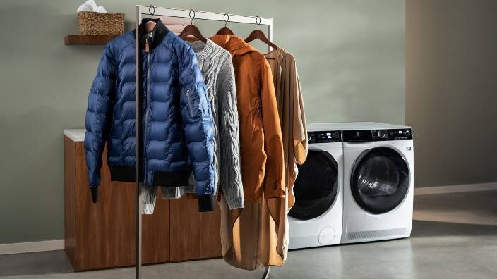 Fire stykker tøj hænger til tørre foran en Electrolux tørretumbler og vaskemaskine.