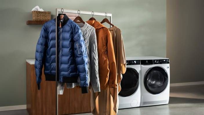 Tøj der hænger pænt på bøjler foran en vaskemaskine og en tørretumbler fra Electrolux.